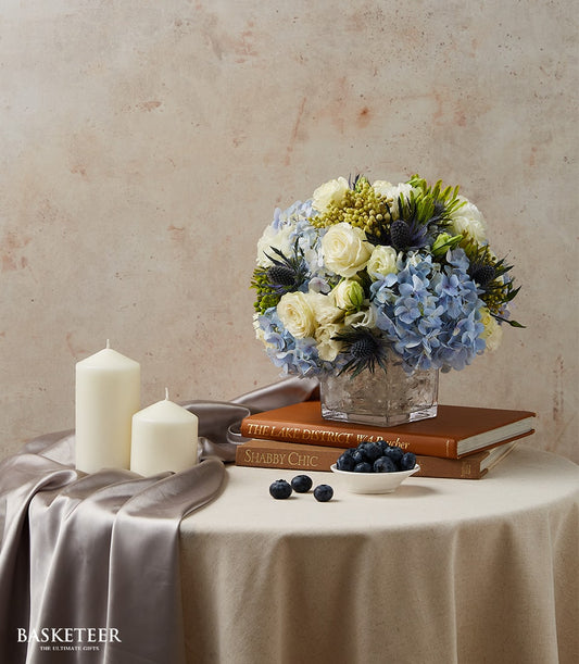 Blue and white hydrangea floral arrangement in glass cube vase for elegant dining table display