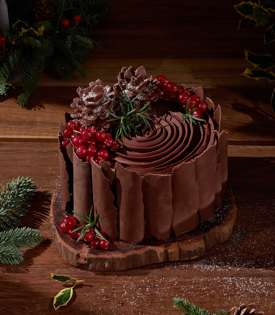 Rich chocolate ganache cake with red currants, chocolate pinecones, and rosemary for festive gifting
