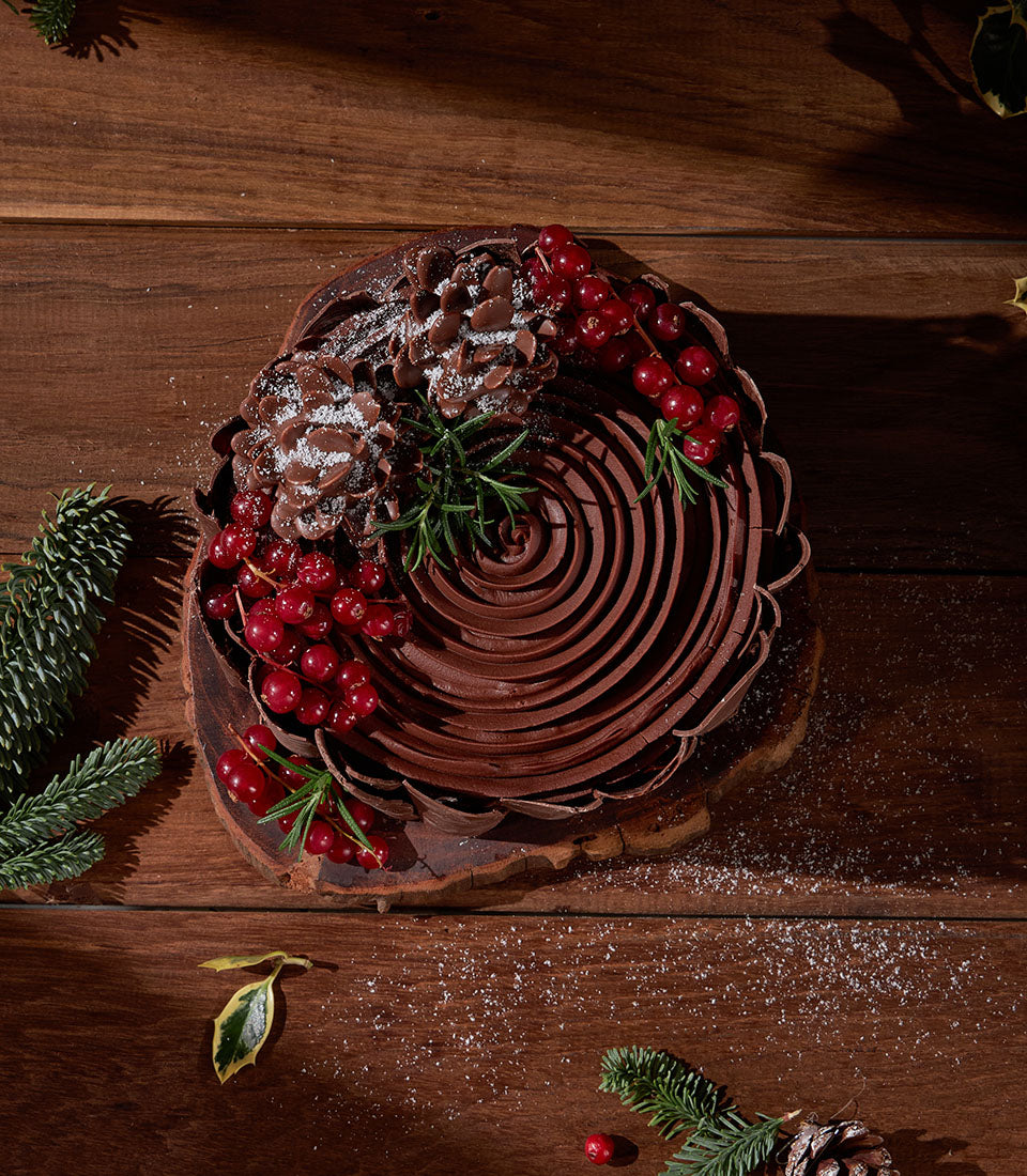 Charlotte Bakery festive cake: Artisan chocolate ganache spiral, decorated with snowy pinecones and bright red currants. Perfect custom cake order in Bangkok.
