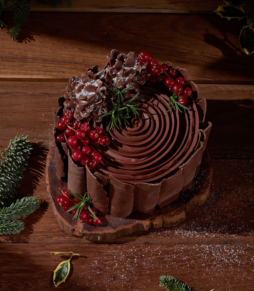 Festive chocolate ganache cake with red currants and rosemary, artisan Christmas dessert on wooden slab
