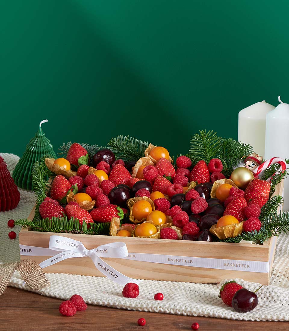 Wooden Christmas fruit gift box with strawberries, raspberries, cherries and physalis on white knit fabric