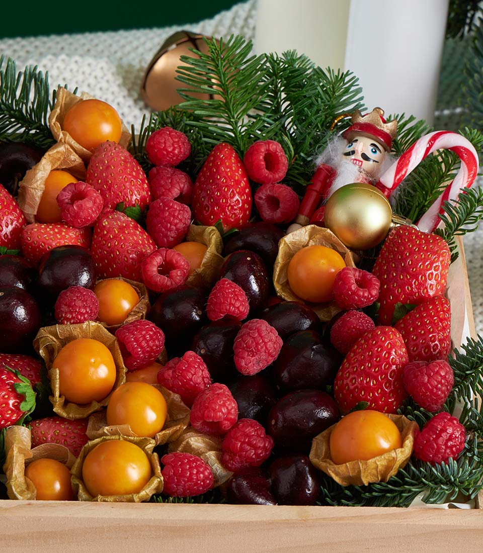 Festive berry fruit gift box with strawberries, raspberries, cherries, and physalis in light wooden crate with holiday