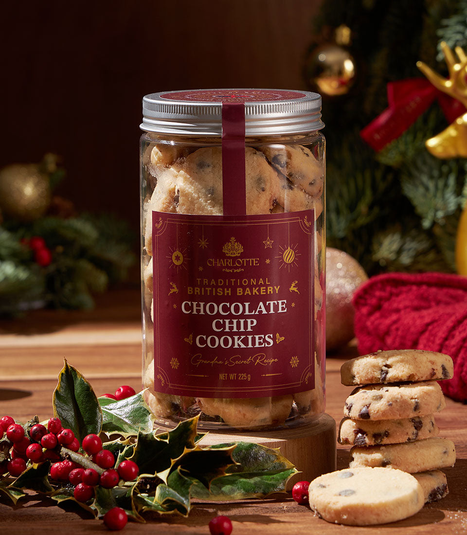 Jar of artisan chocolate chip cookies from Charlotte Bakery, a British bakery in Thailand. Festive holiday decorations and loose cookies on a wooden surface.