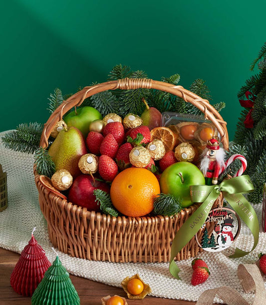 Festive wicker fruit basket with fresh apples, pears, oranges, strawberries, gold Ferrero chocolates, and Christmas ornaments