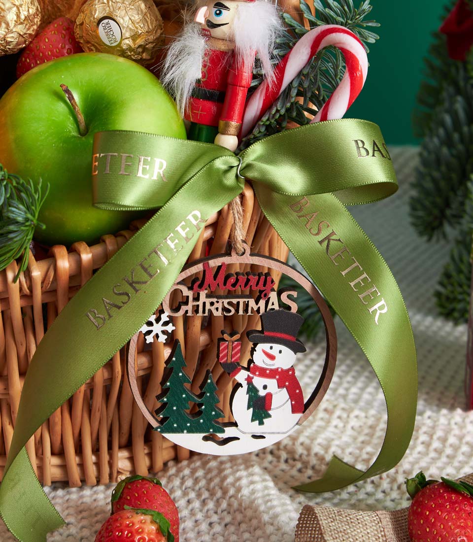 Christmas fruit basket with Ferrero Rocher, fresh apples, strawberries, and wooden snowman ornament in woven wicker
