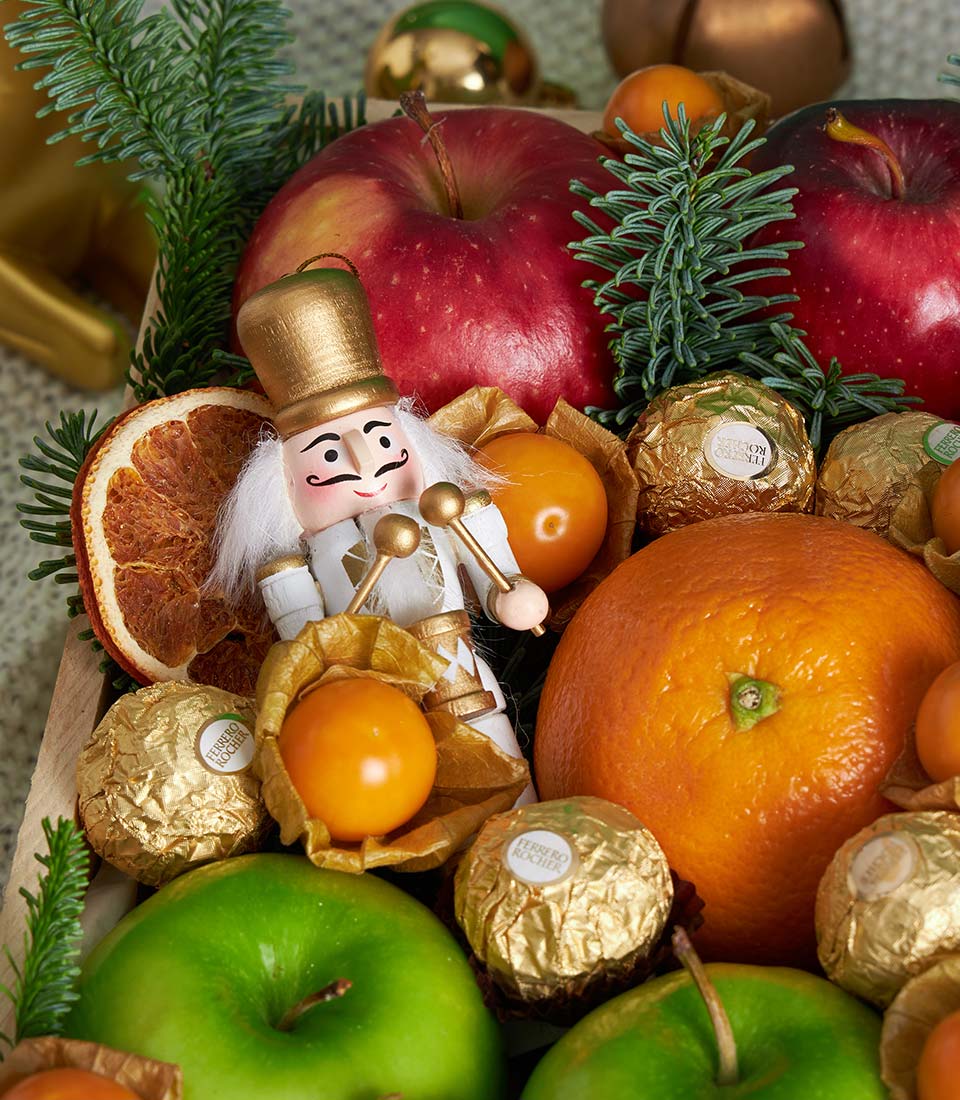 Luxury festive mixed fruit gift box with apples, oranges, physalis, Ferrero Rocher chocolates, and wooden nutcracker in
