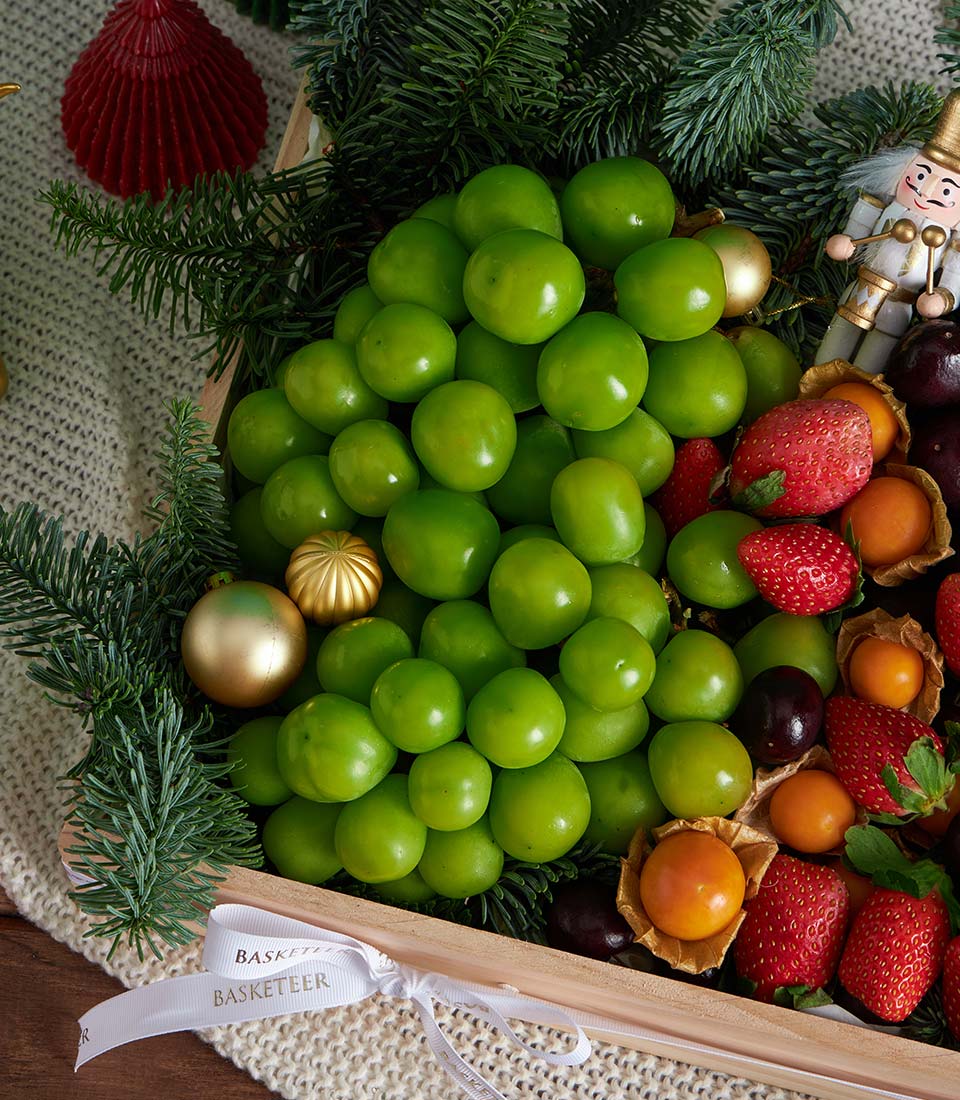 Premium festive fruit gift box with green plums, strawberries, and physalis arranged as Christmas tree with gold ornaments