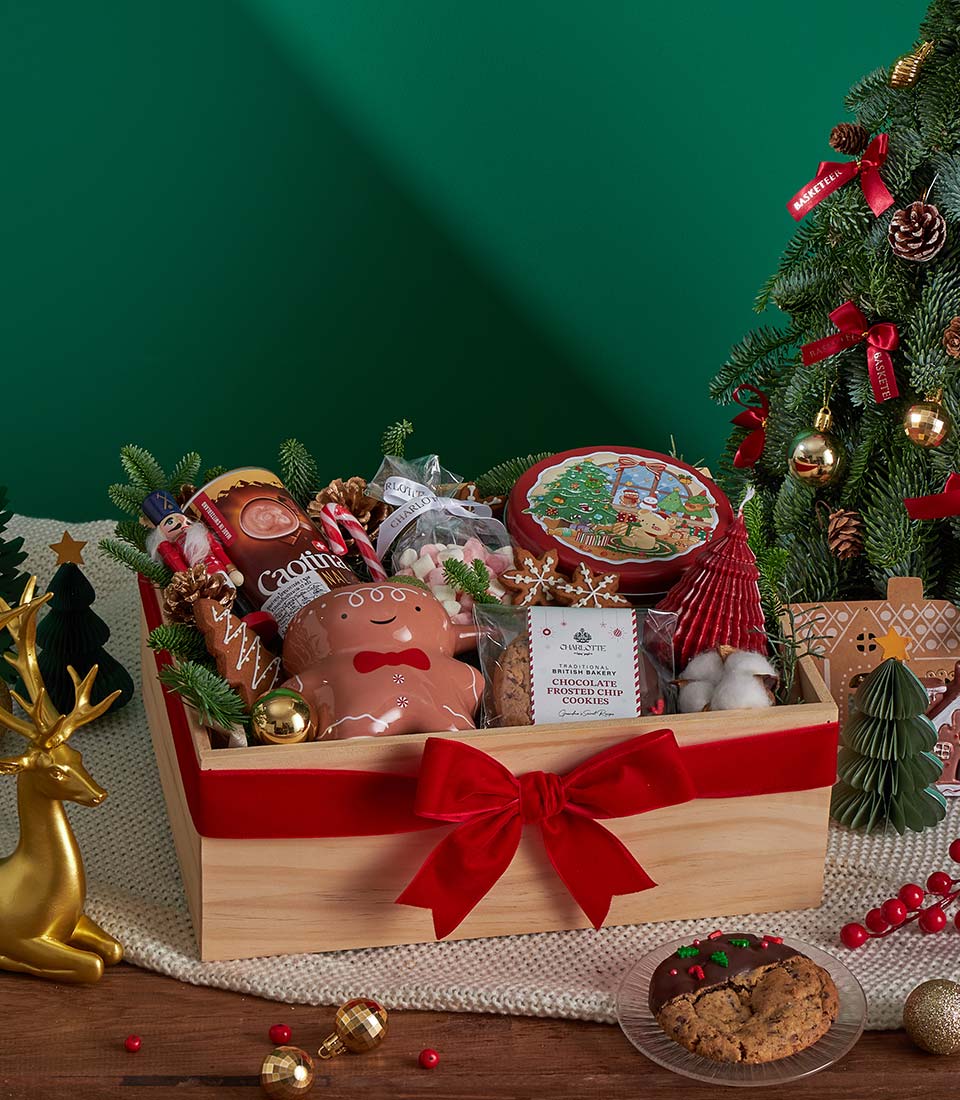 Festive wooden crate gift box with hot chocolate, gingerbread mug, Christmas cookies, and candle tied with red velvet ribbon