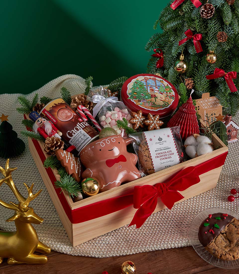Festive wooden gift box with gingerbread mug, hot chocolate, marshmallows, and chocolate frosted cookies tied in red velvet