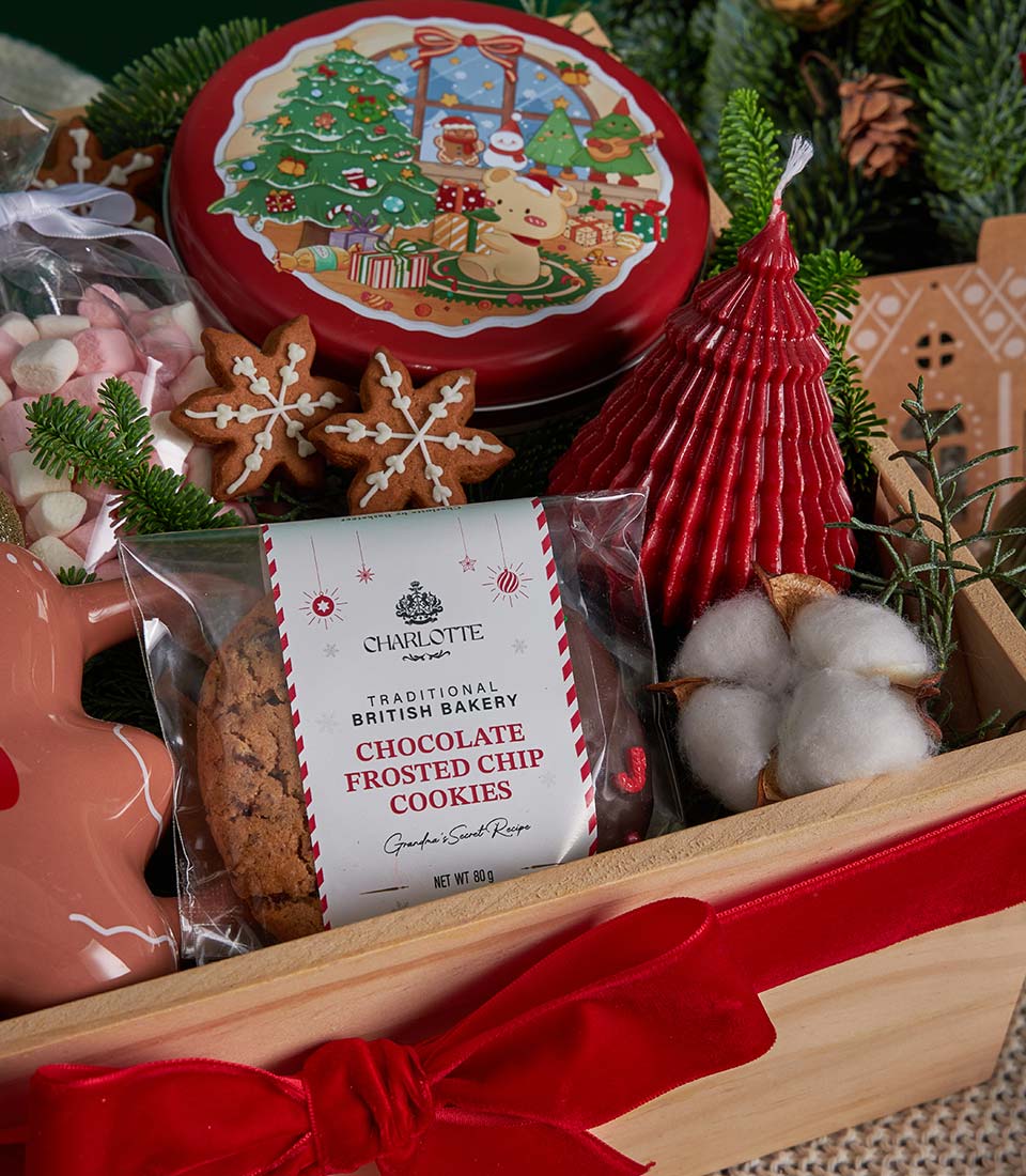 Festive Christmas gift box with gingerbread cookies, hot chocolate, candle and evergreen sprigs in wooden crate