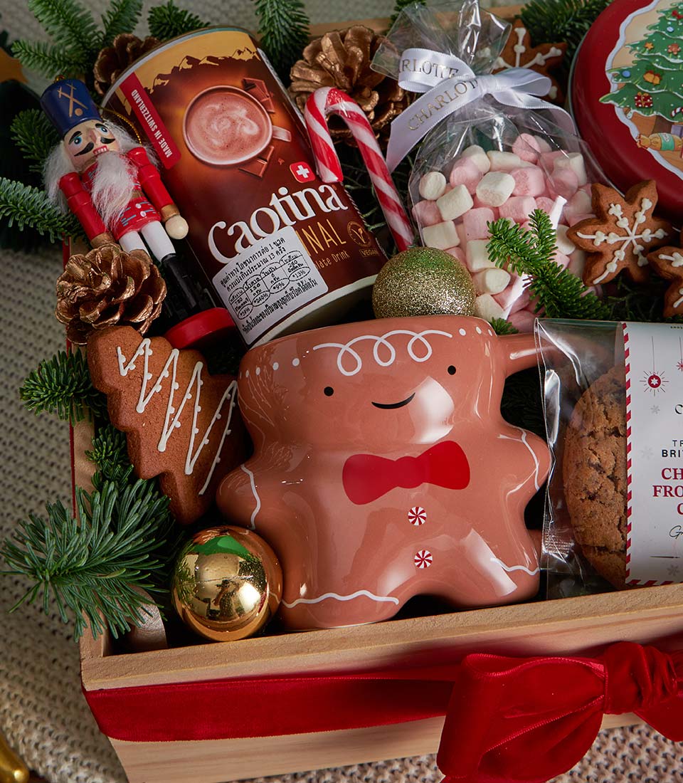 Festive Christmas gift box with gingerbread mug, hot chocolate, marshmallows, cookies and candle among pine branches