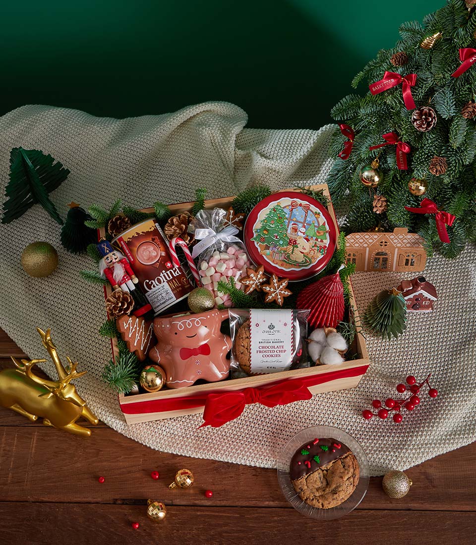 Festive Christmas gift box with hot chocolate, gingerbread cookies, marshmallows, and candle in wooden crate with red ribbon