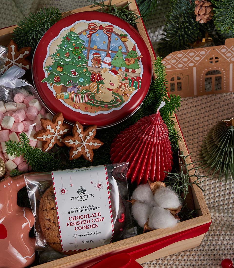 Festive Christmas gift box with gingerbread cookies, hot chocolate, chocolate chip cookies, marshmallows, and red tree candle