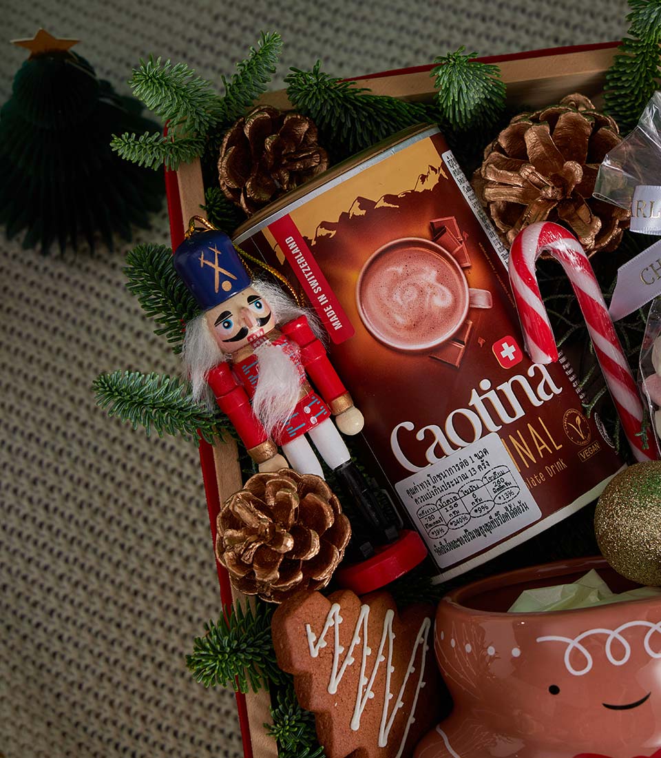 Festive Christmas gift box with hot chocolate, candy cane, gingerbread cookies, and wooden nutcracker ornament