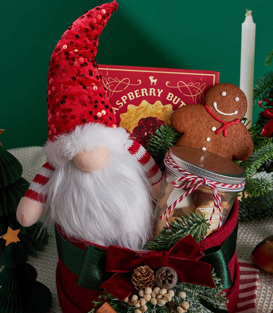 Red Christmas gift basket with festive gnome, gingerbread cookies, and star-shaped treats in glass jar