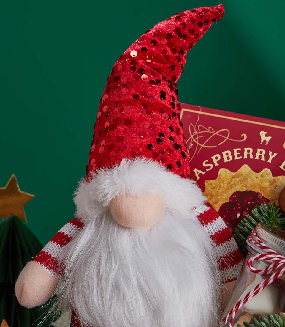 Christmas gnome, raspberry cookie box, and festive treats jar on dark green background