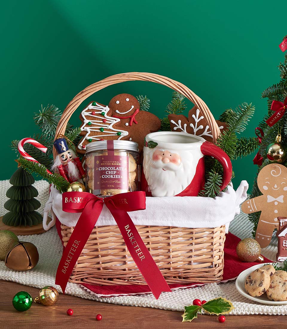 Wicker Christmas gift basket with gingerbread cookies, chocolate chip jar, and Santa mug tied with red ribbon