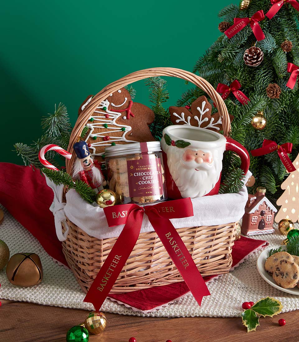 Woven Christmas gift basket with gingerbread cookies, chocolate chip cookies jar, Santa mug, and festive nutcracker