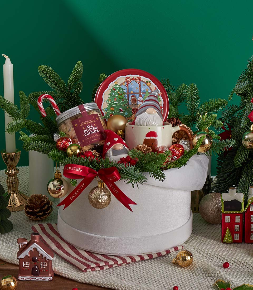 Festive Christmas biscuit and chocolate gift basket with Santa mug, cookies, and holiday ornaments in white box with red