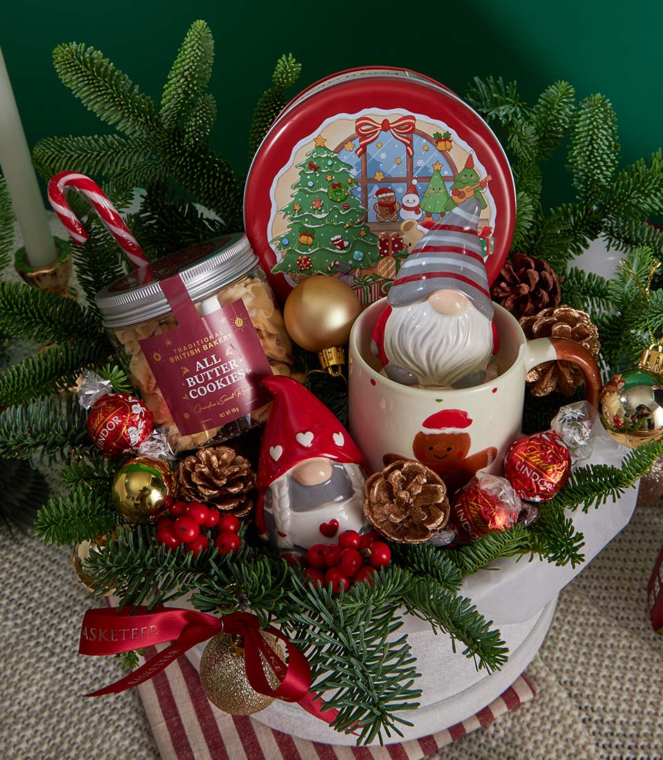 Festive red and white Christmas gift basket with butter cookies, chocolate tin, gingerbread mug, and holiday ornaments