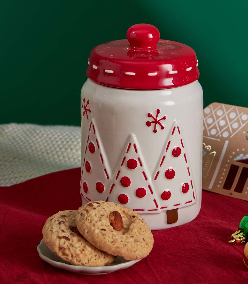 Festive white ceramic Christmas cookie jar with red lid and holiday tree designs, paired with almond-topped butter cookies