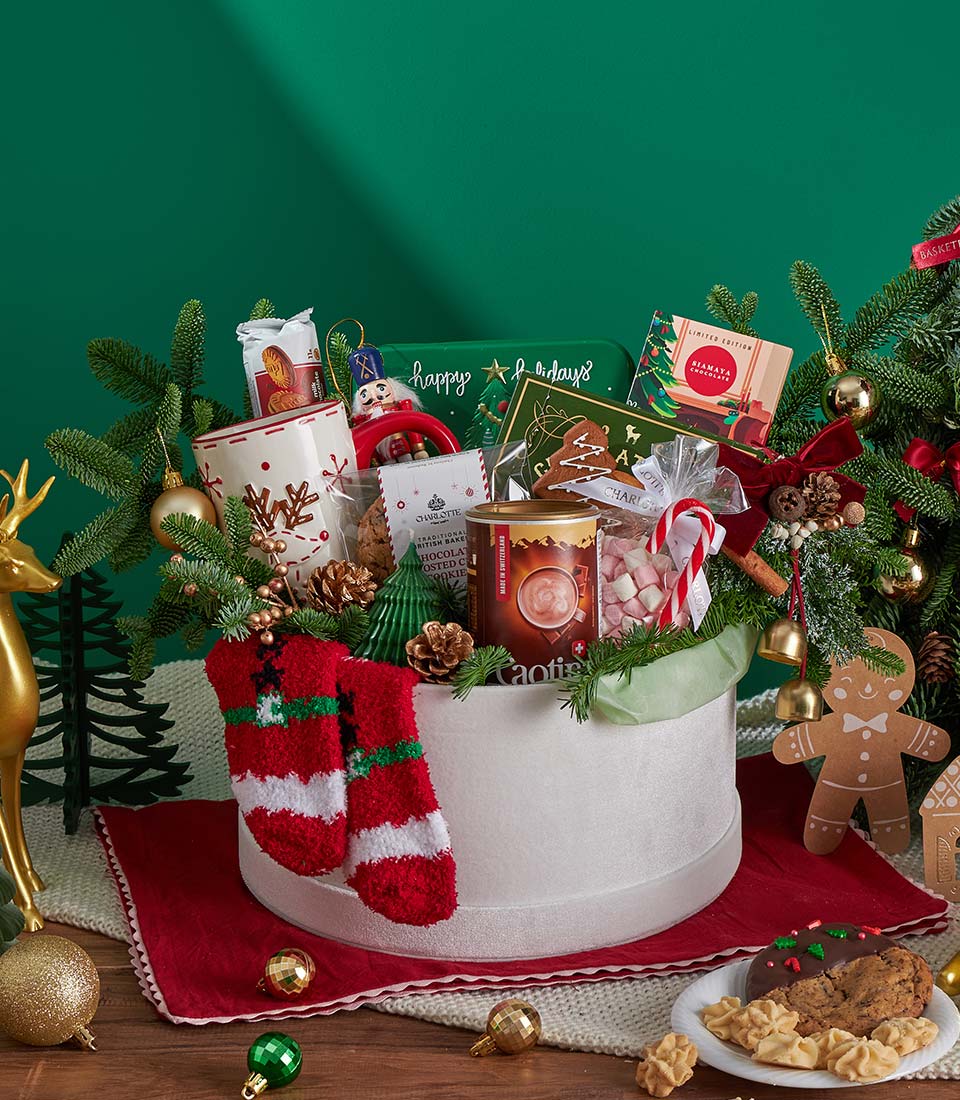 Festive Christmas gift basket with hot chocolate, cookies, reindeer mug, fuzzy socks, and holiday treats on dark green
