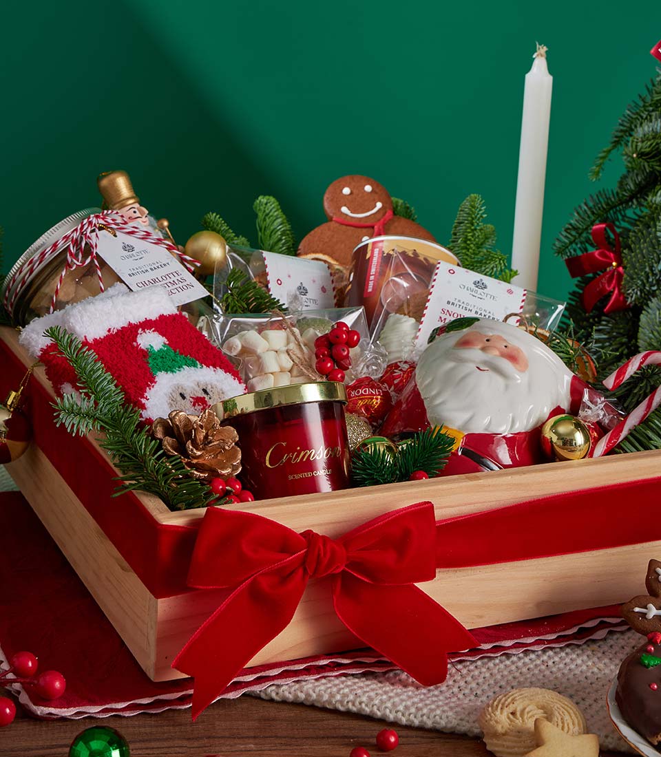 Festive Christmas gift basket with holiday cookies, hot chocolate, marshmallows, and festive decorations in wooden crate