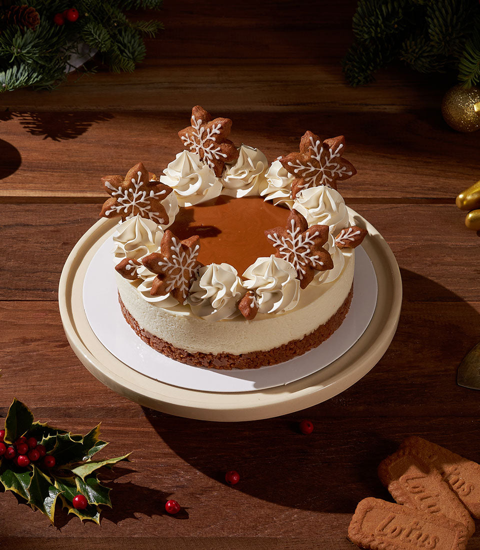 Gingerbread Biscoff cheesecake with caramel top, cream swirls, and snowflake cookies on festive cake stand