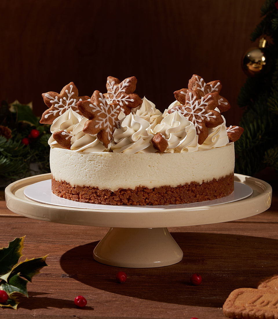 Gingerbread Biscoff Christmas cheesecake with whipped cream and snowflake cookies on ceramic stand