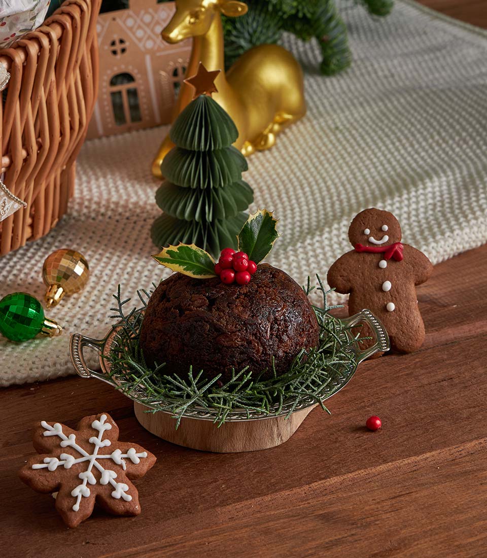 Luxury Christmas pudding and gingerbread cookies with holly garnish in festive gift basket setting
