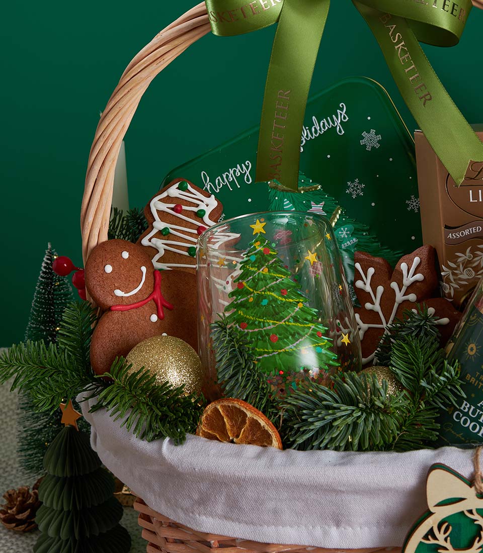 Deluxe Christmas gift basket with gingerbread cookies, chocolate, festive glass, and holiday decorations in woven basket