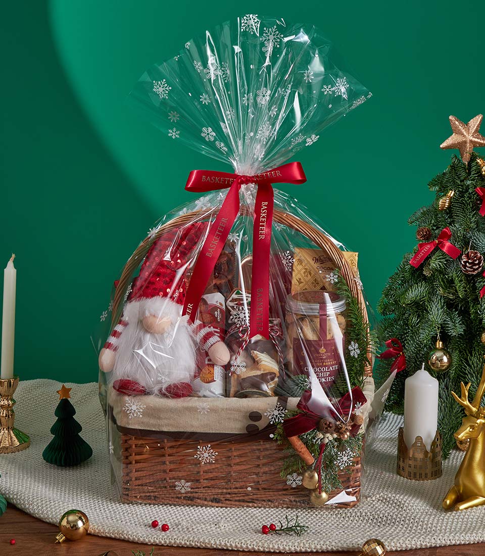 Festive Christmas gift basket with chocolate chip cookies, hot cocoa, and gnome plush toy wrapped in snowflake cellophane