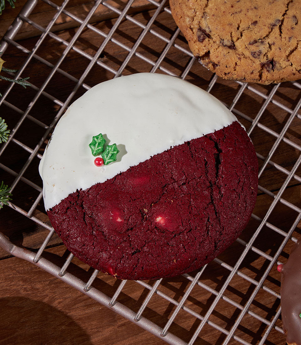 Festive red velvet Christmas cookies with white icing and holly decoration on cooling rack
