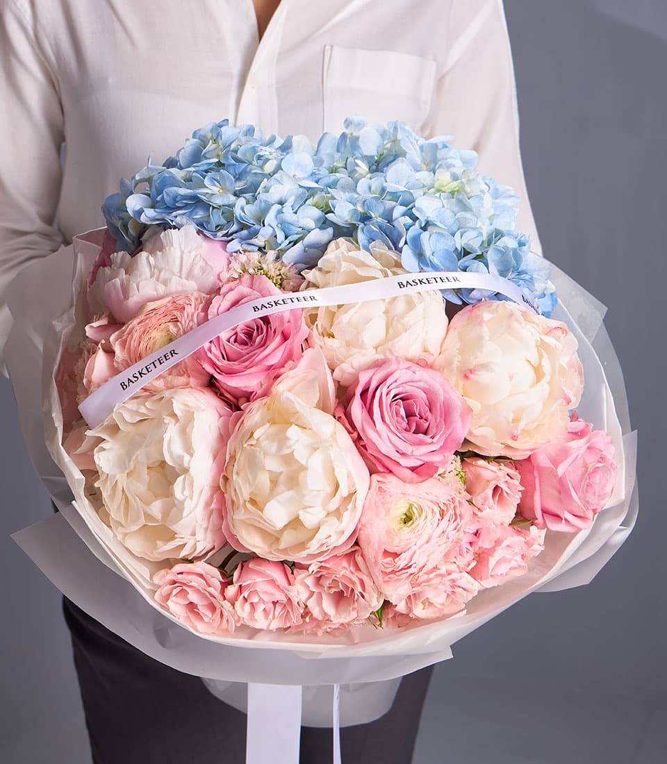 Pastel Harmony Mixed Bouquet with blue hydrangeas, cream peonies, and pink roses in luxe wrapping