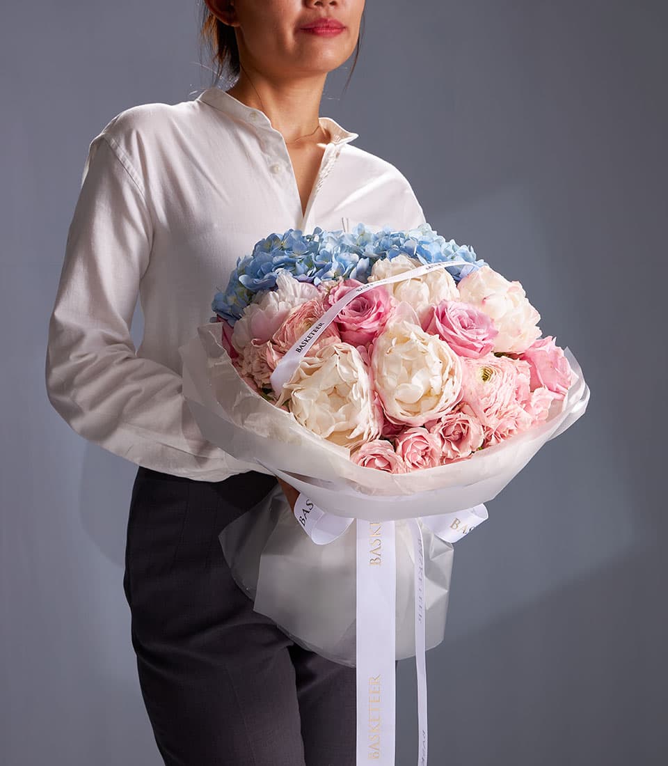 Pastel Harmony bouquet of hydrangeas, roses, and peonies wrapped in white cellophane with gold-lettered ribbon
