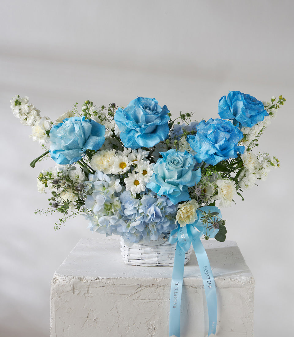 Blue and white rose basket with hydrangeas, daisies, and ribbons in white woven basket