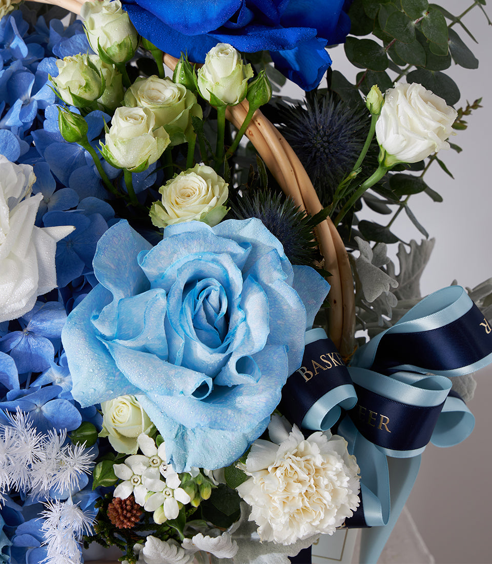 Blue and white rose basket with hydrangeas, carnations, and thistle in woven arrangement