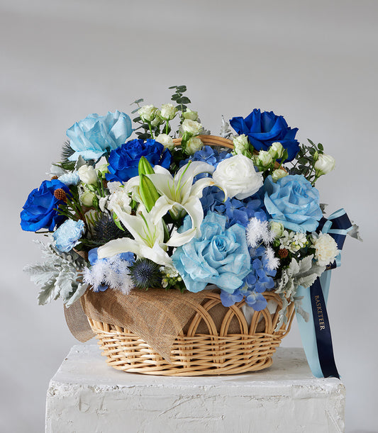 Premium blue and white rose basket with hydrangeas, lilies, and silvery foliage in woven wicker