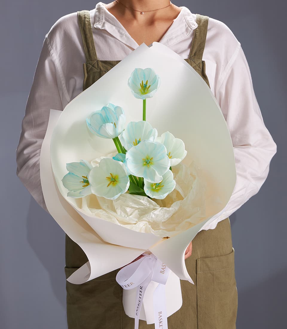 Pastel blue and white tulip bouquet with yellow stamens, wrapped in white paper and white ribbon