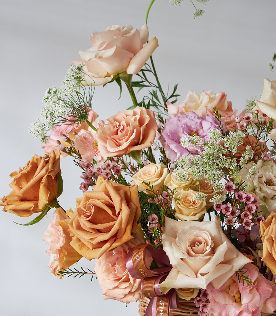 Caramel and blush roses with purple lisianthus in woven lilac basket