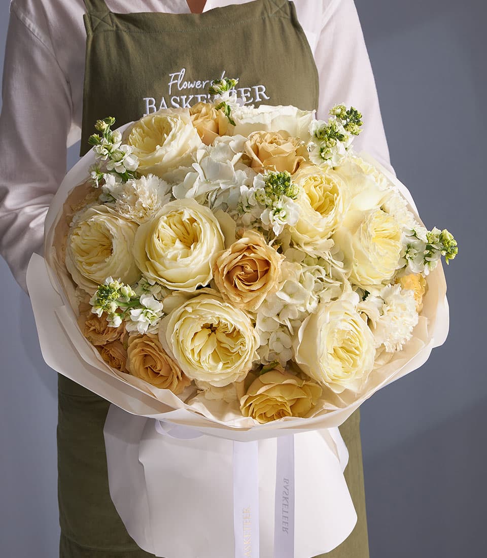 Ivory garden rose and white hydrangea bouquet with cream and peach roses, wrapped in white paper with ribbon