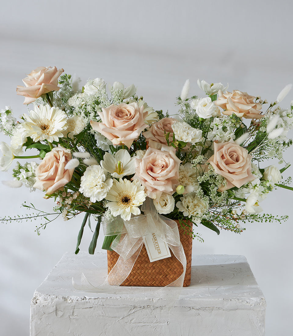 Cream roses and white gerberas in a woven basket with gold ribbon, luxury flower gift arrangement