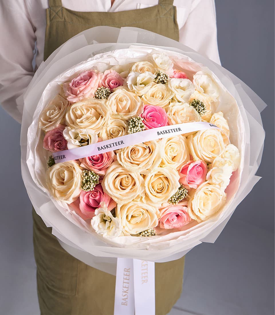 Cream and pink rose bouquet with white filler flowers, wrapped in tissue paper with white ribbon