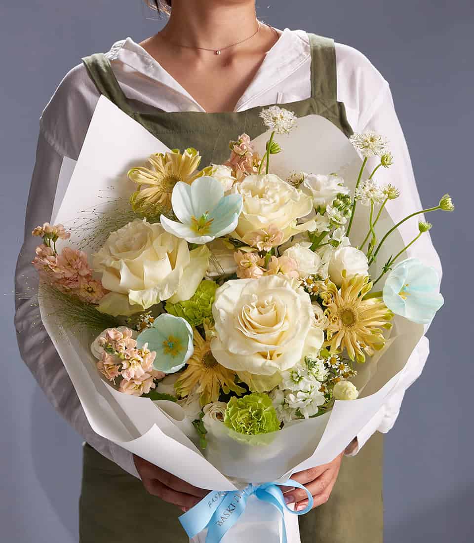 Ivory roses, blue anemones and champagne blooms in elegant pastel bouquet with white wrapping