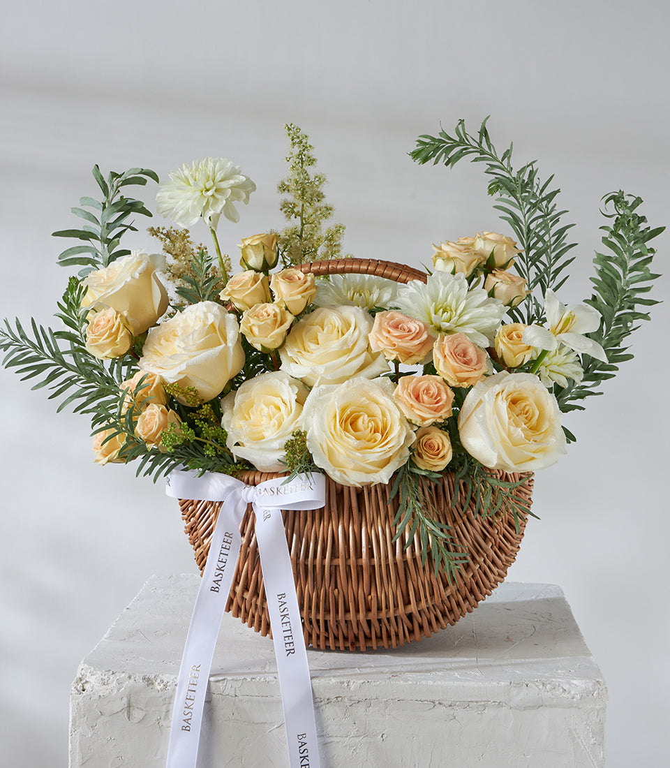 Ivory and peach spray roses with white dahlias in woven wicker basket, fresh flower arrangement for gifting