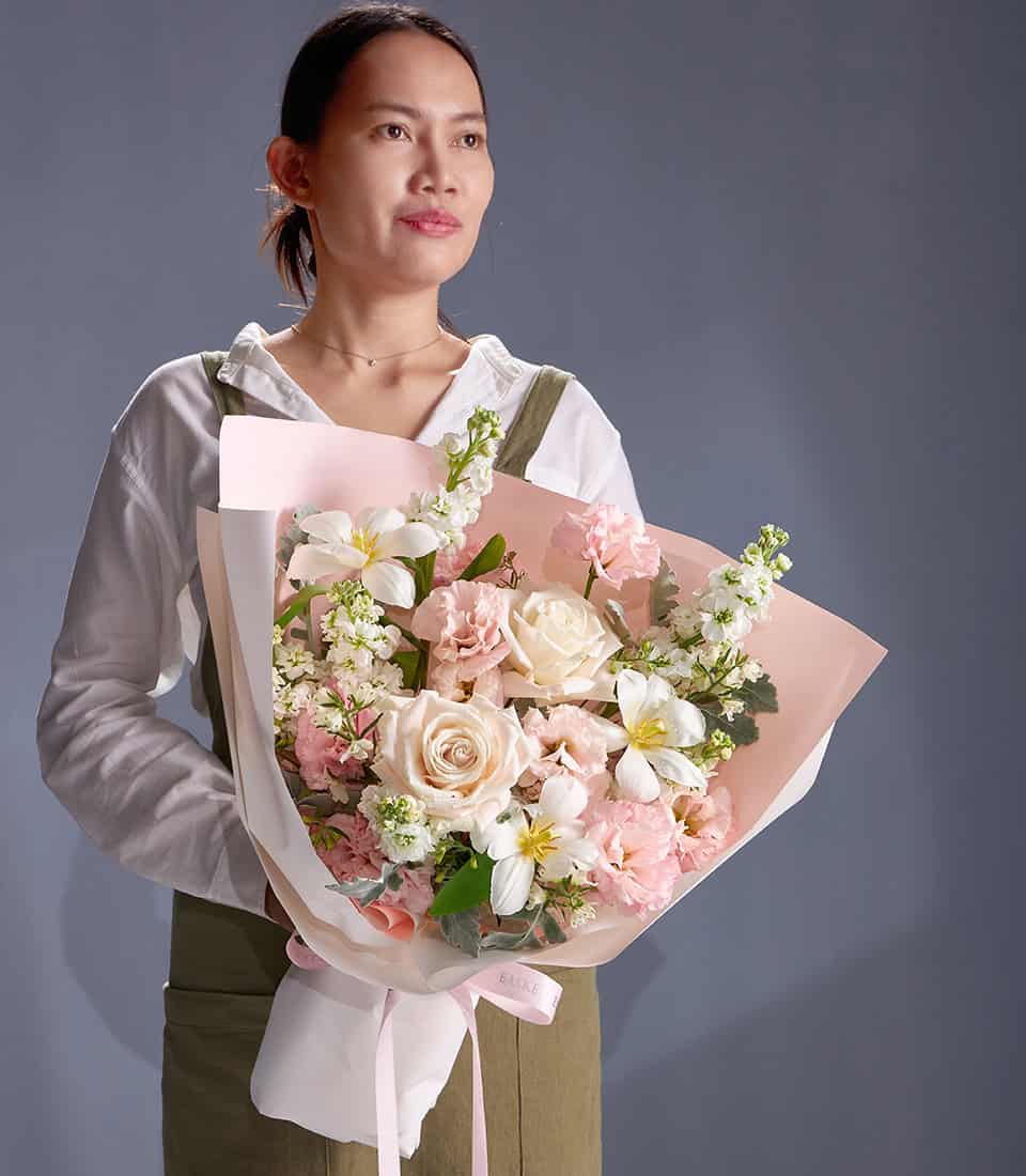 Ivory and blush rose bouquet with white freesia and soft pink filler flowers, wrapped in pastel paper