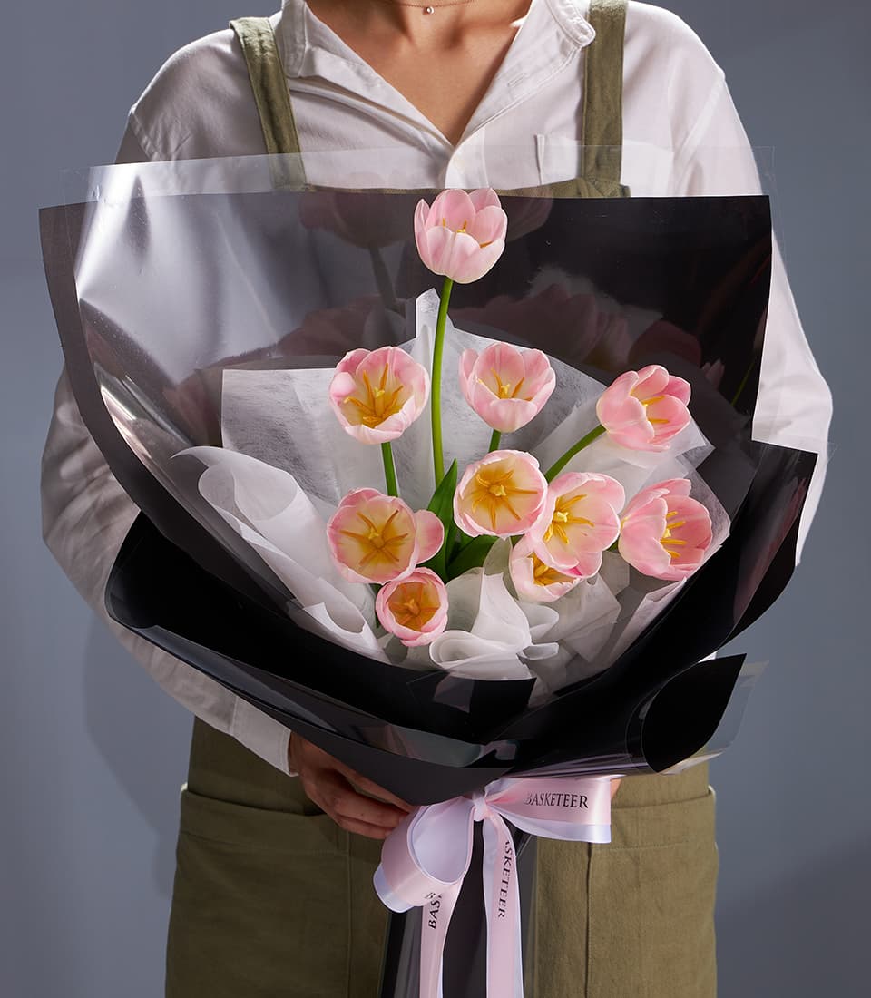 Pastel pink tulip bouquet with yellow centers, wrapped in cellophane and tied with pink ribbon