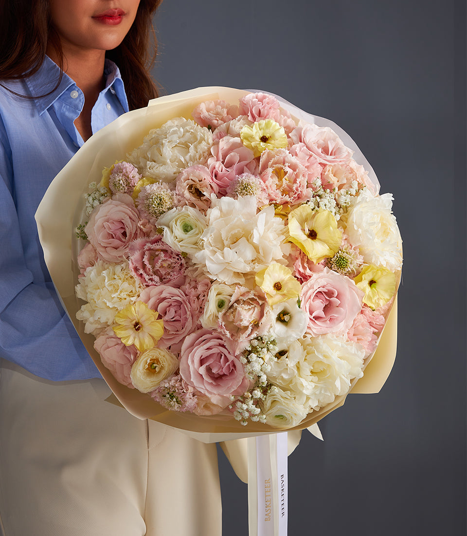Romantic Blossom Bouquet of pale pink roses, cream carnations, and soft yellow blooms wrapped in light cream paper with
