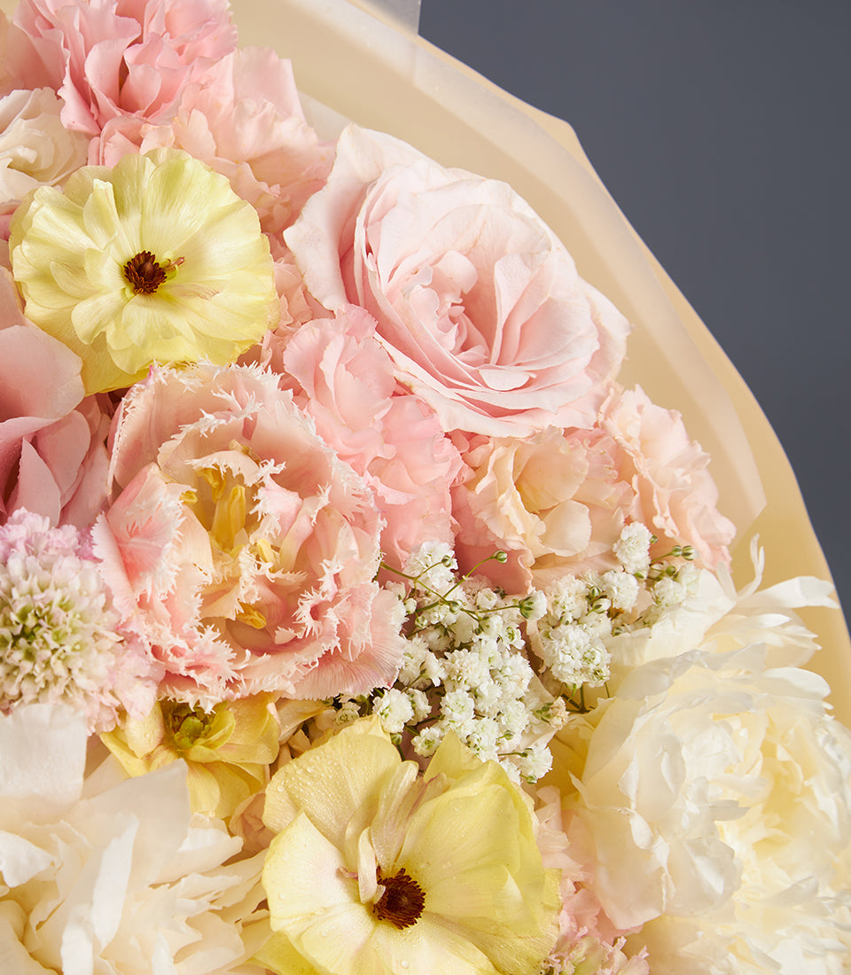 Romantic Blossom Bouquet with pink roses, carnations, yellow ranunculus, and baby's breath wrapped in cream paper