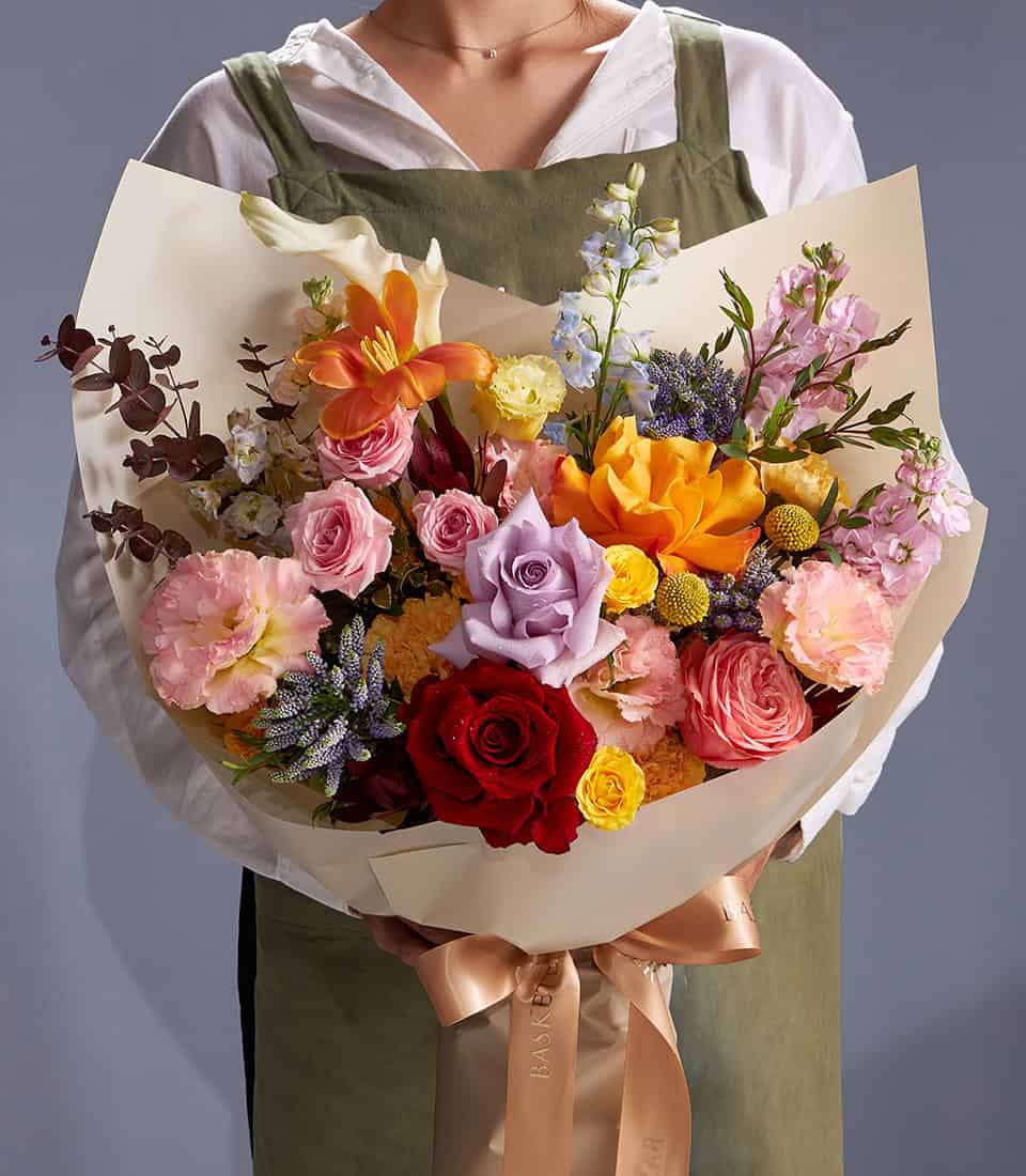 Mixed orange lilies, roses and pastel wildflowers in beige paper with satin ribbon